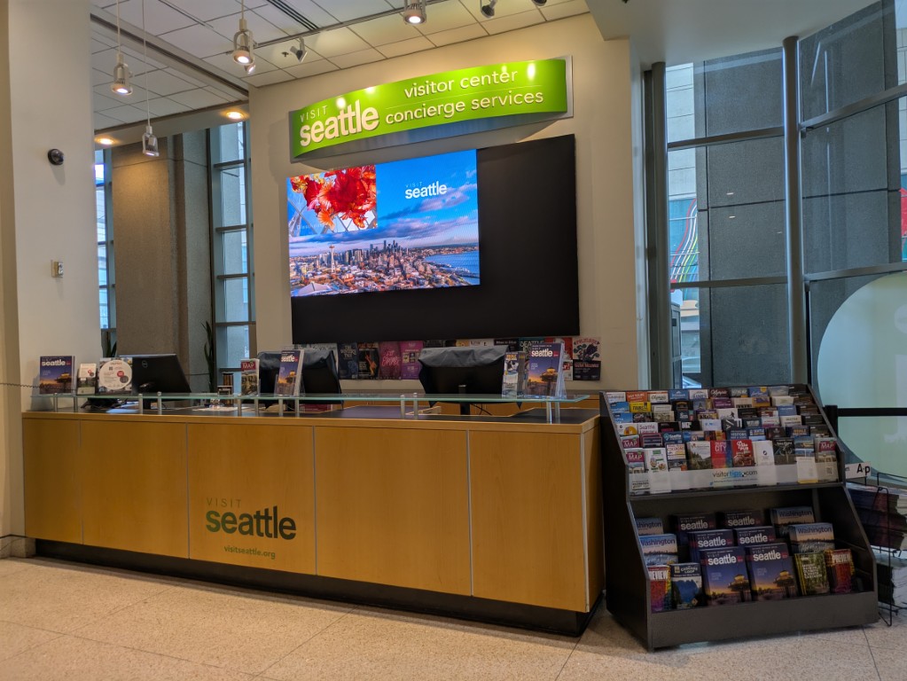 Visit Seattle visitor center and concierge desk inside the Arch, empty — no staff, screens running, March 2025